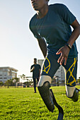 Coach timing young male amputee athlete running in grass