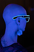 Woman with shaved head wearing neon glasses in blue light