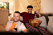 Happy gay male couple with wine and popcorn watching movie