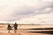Couple holding hands walking on sunny tranquil winter beach