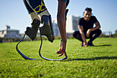 Coach watching male amputee athlete stretching in sunny park