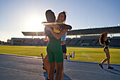 Happy female track and field athletes hugging on sunny track