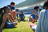 Young athletes resting and talking on sunny stadium lawn