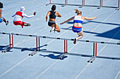 Female athletes jumping hurdles on sunny track