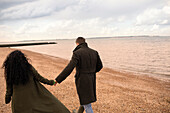 Affectionate couple holding hands walking on winter beach