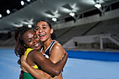 Happy athletes hugging on track at night