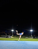 Female athlete throwing discus at stadium at night