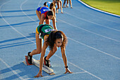 Female athletes ready at starting blocks on blue track