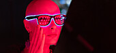 Woman with shaved head in neon glasses in red light