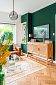 Sideboard against dark green wall in living room decorated in natural tones