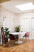 Classic table and chairs, houseplants and standard lamp in room with patterned wallpaper