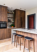 Bar stools at kitchen island with stone top and cabinets with wooden fronts