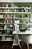 White desk, shell chair and bookshelves in study with green wall
