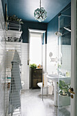 Small bathroom with white wall tiles below blue walls and ceiling, wire shelving unit and shower area in foreground