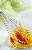 Glass bowl with red wine vinegar-olive oil vinaigrette and a whisk
