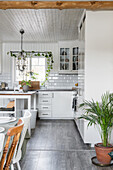 White country-house kitchen with island counter and dining area in foreground