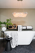 Freistehende Badewanne, darüber elegante Leuchte im Badezimmer mit beigefarbener Wand
