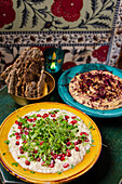 Bowl of middle eastern hummus and aubergine spread with pomegranate seeds and micro herbs