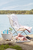 Liegestuhl, Korb und Tablett mit Wellness- und Badeutensilien am See