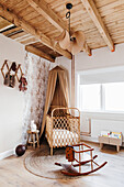 Babybett mit Baldachin im Kinderzimmer mit hoher Holzdecke