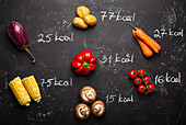 Different vegetables on black stone background and chalk wrote calories quantity