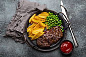 Grilled beef steak with potato chips french fries and green peas served with red tomato sauce