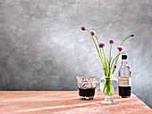 Chive blossoms in a glass vase next to homemade elderberry vinegar