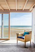 Yellow armchair next to open patio door with view of beach and sea
