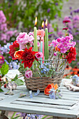 Basket with dahlia, rose, phlox and widow flower blossoms in bottles and candles as table decoration, rose blossom and hydrangea blossoms
