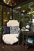 Round table, armchair with sheepskin and animal-print cushion in conservatory