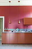 Kitchen base units below pendant lights in front of red wall