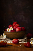 A bowl of red plums with a few flowers for garnished