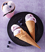 Homemade blueberry ice cream in waffle cones and paper cups