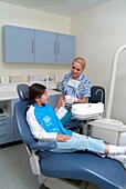 Dental nurse handing girl in dentist chair a cup