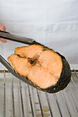 Holding salmon steak with tongs over grill rack