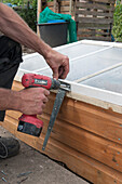 Man constructing a cold frame with a drill