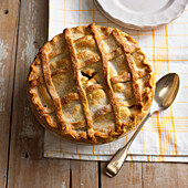 Apple pie with spoon and plates nearby, on folded tea towel
