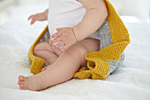 Baby girl sitting on bed wearing knitted hooded blanket