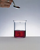 Clear liquid dripping into a beaker containing red liquid