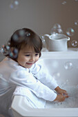 Young girl in pyjamas making bubbles in basin