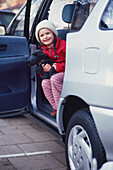 Smiling girl looking out from the back of an open car door