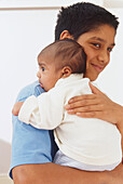 Smiling teenage boy holding a baby in a white outfit