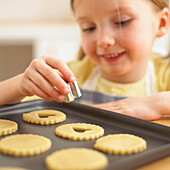 Girl holding cookie cutter over tray of cookies