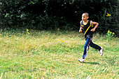 Boy in tracksuit bottoms and vest jogging on grass