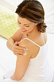 Woman rubbing cream into left upper arm using right hand