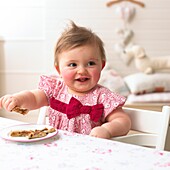 Baby girl picking up slices of toasted fruit loaf from plate