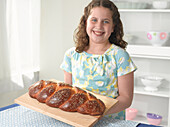 Girl holding braided challah loaf on chopping board