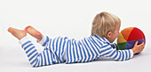 Boy in striped pyjamas lying on floor holding ball