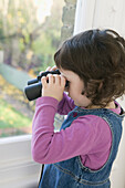 Girl standing by window looking through binoculars