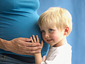 Boy leaning his head against pregnant woman's belly